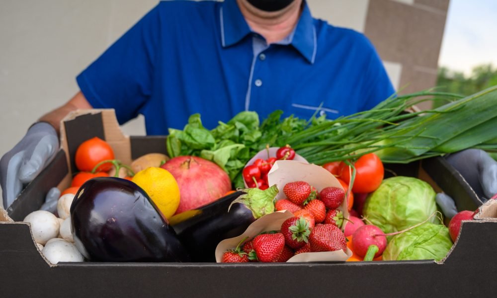 Delivery man in mask holding fresh vegetables box. Home delivery during quarantine